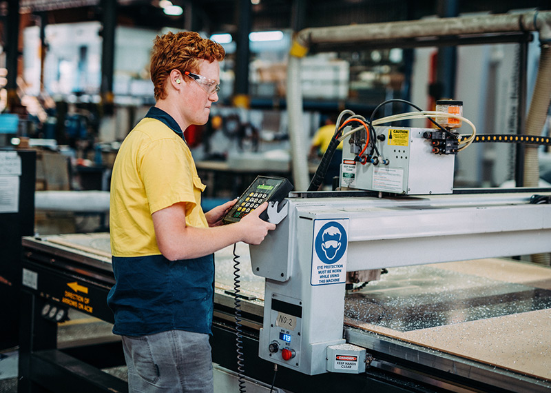 A man wearing protective goggles uses machinery.