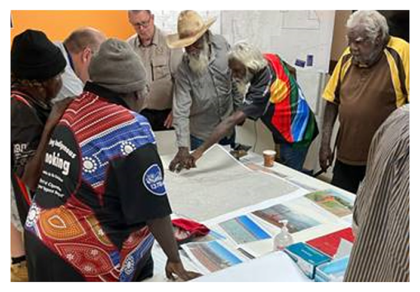 A photo showing participants at a mining exploration consent meeting including Traditional Owners and CLC staff standing around a table and looking at a map on the table. Some participants are pointing to features on the map.