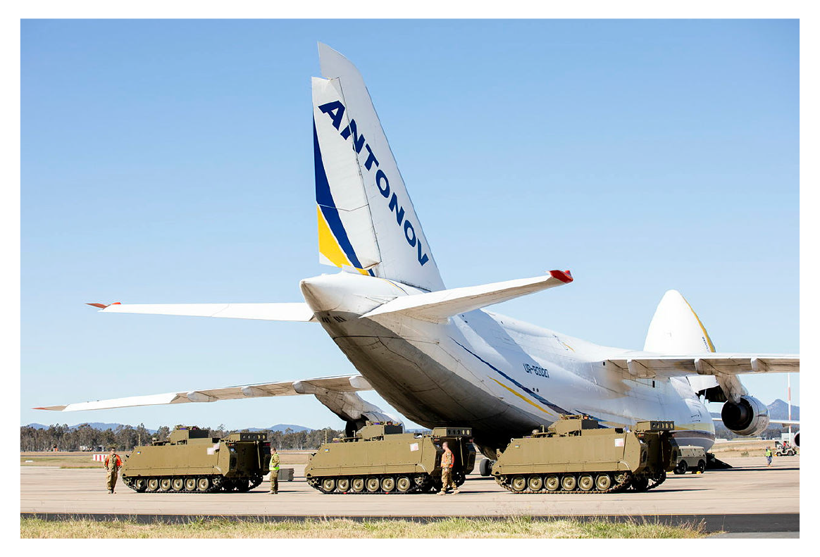 This is a photograph showing M113AS4 armoured personnel carriers waiting to be loaded onto an Antonov An-124 aircraft at RAAF Amberley