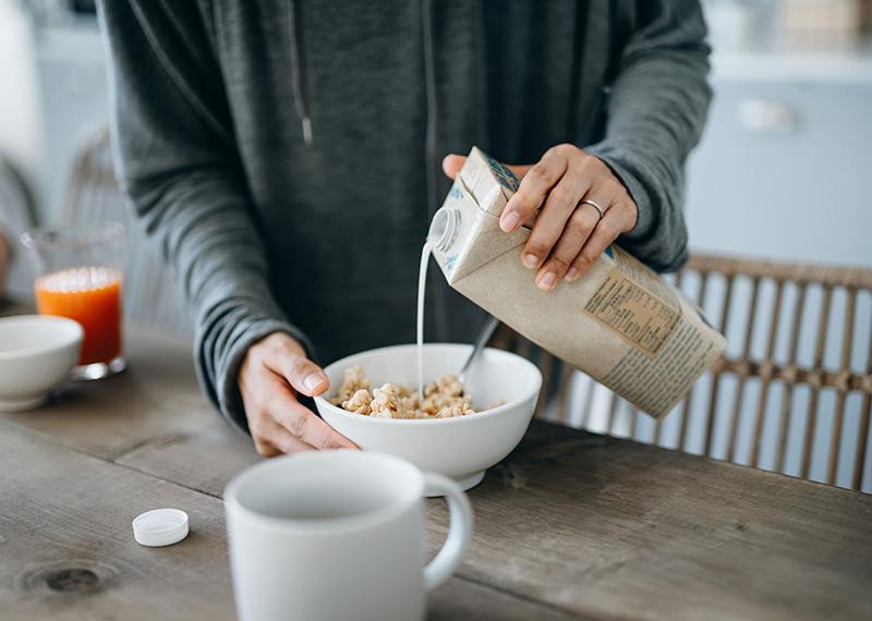A close up photograph of a person pouring milk into a bowl of cereal. 