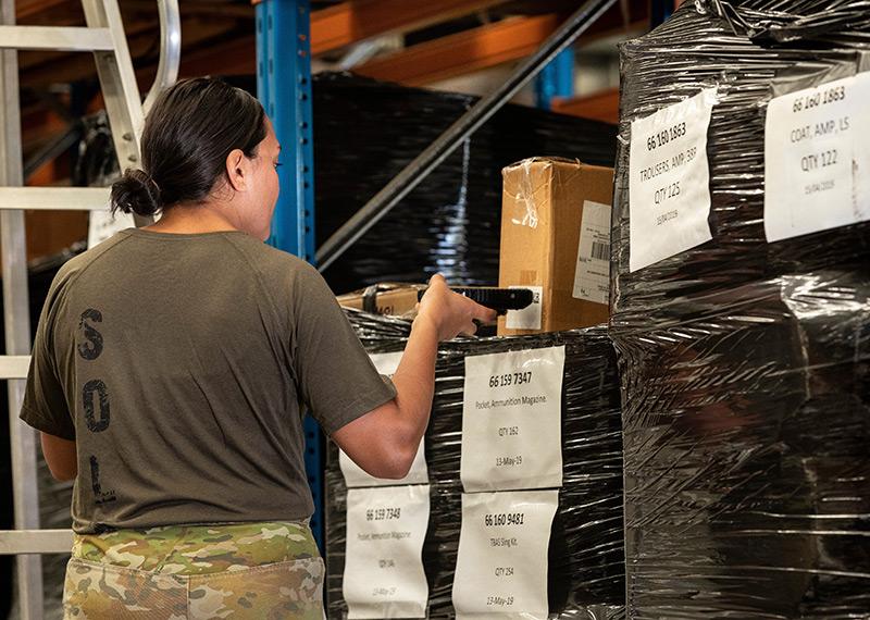 A woman wearing army clothing scans a box's barcode in a warehouse.
