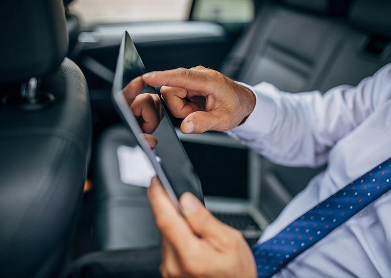 Person wearing a suit sitting in a car using a digital tablet device