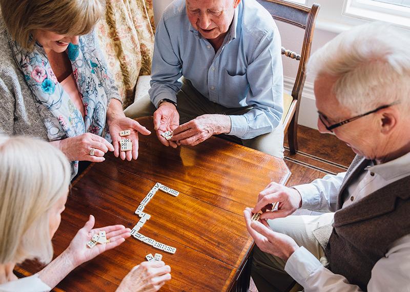 A group of elderly people sit around a table playing dominos