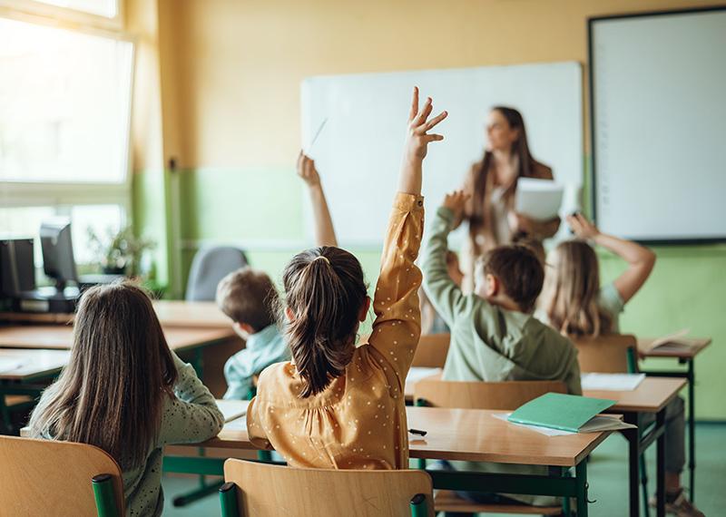 Students raising hands while teacher asking them questions in classroom